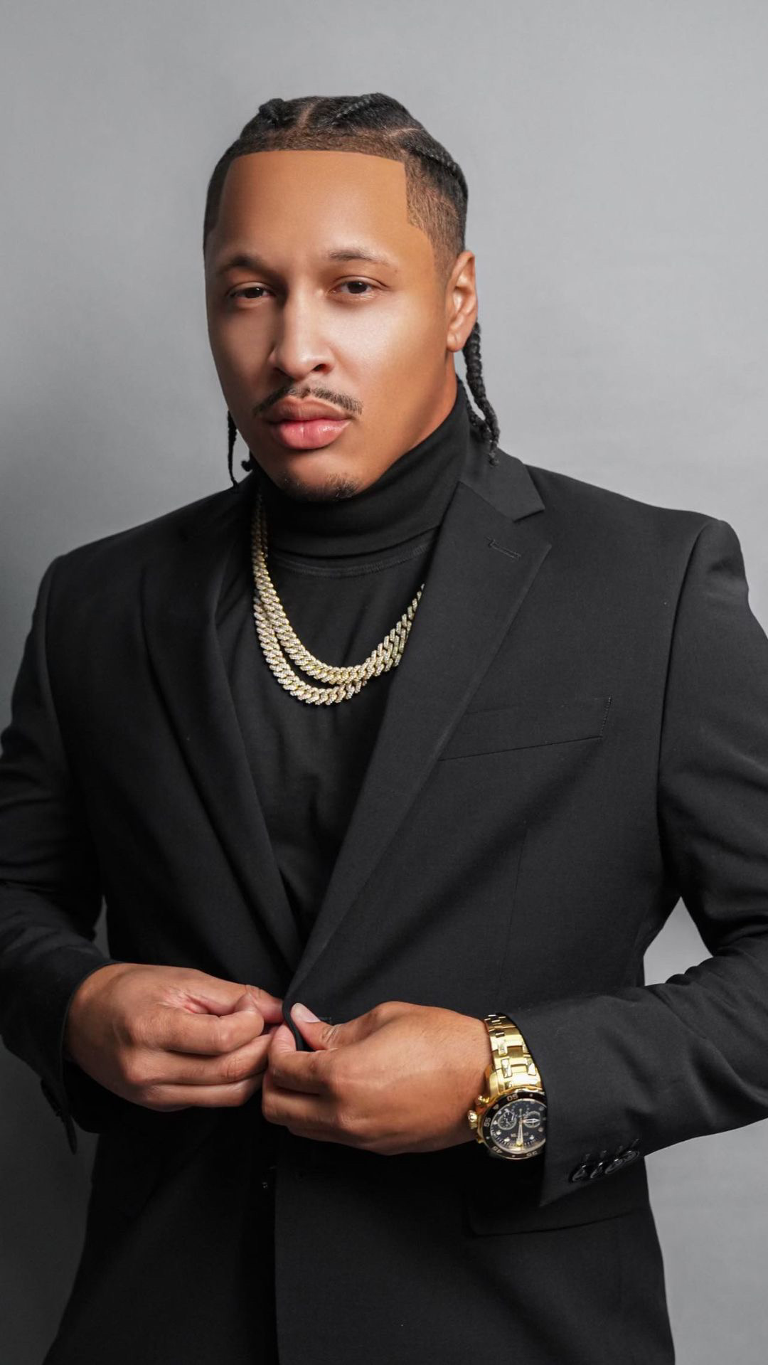 Worth Too Much in a black suit and gold chains, buttoning his jacket