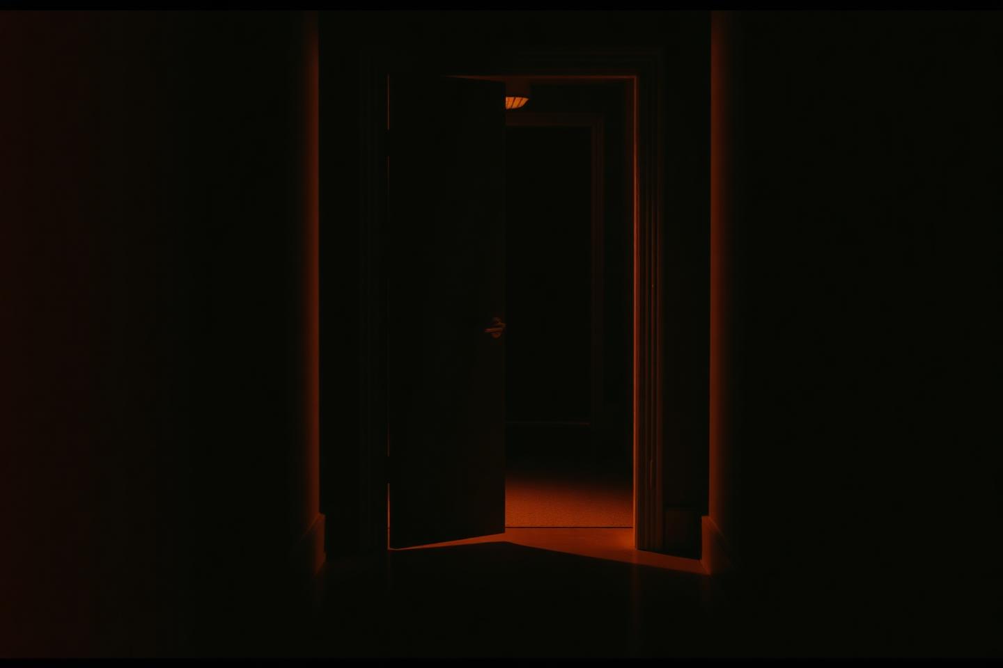 An open door at the end of a dark hallway with warm light spilling out